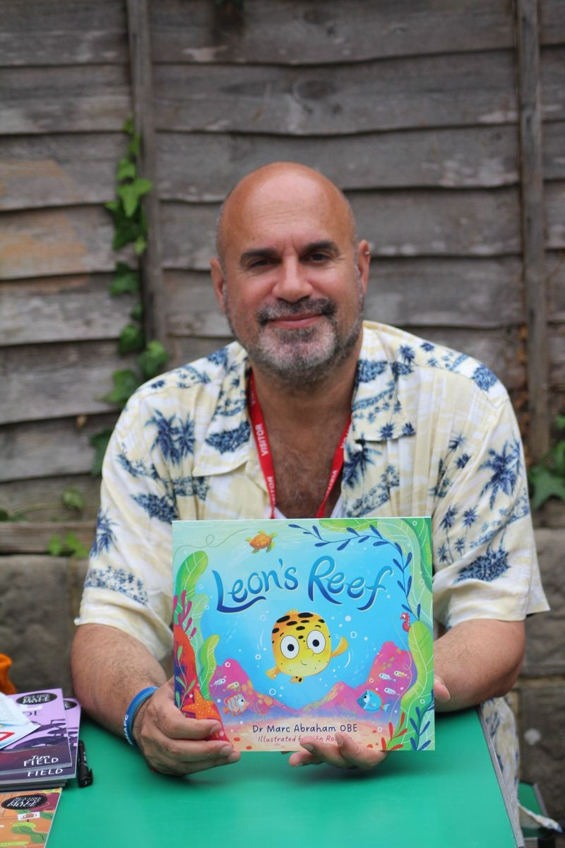 Dr Marc Abraham OBE holding a copy of Leon's Reef